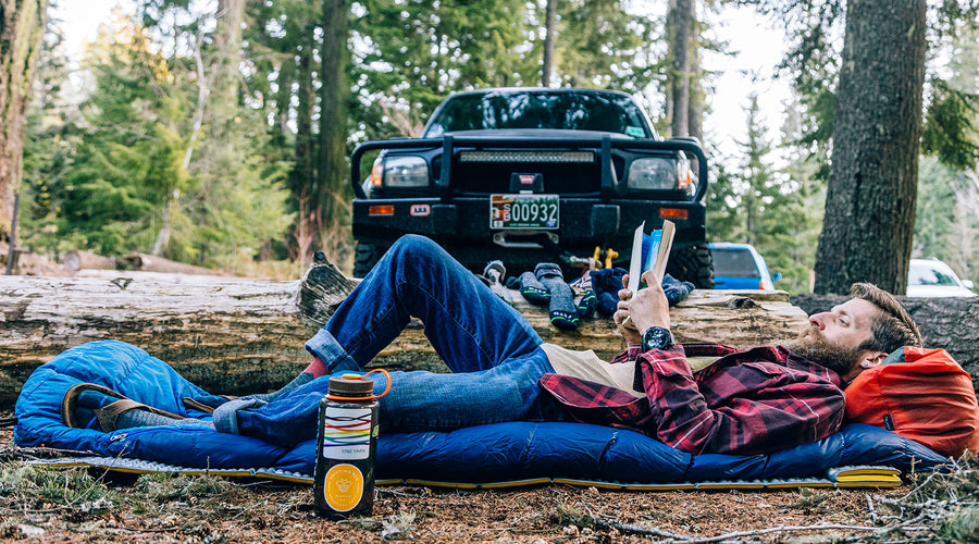 a man laying on a sleeping bag reading a book